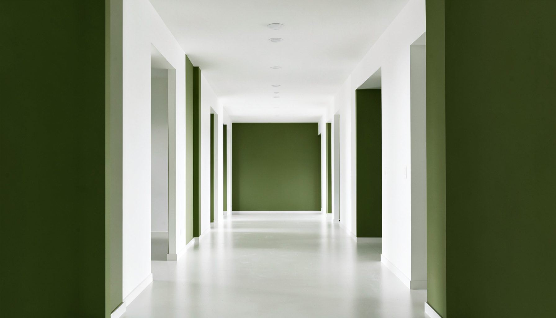 Fotografía arquitectónica simétrica de un pasillo luminoso en tonos blancos y verde oliva, con columnas ordenadas y una atmósfera tranquila y ordenada